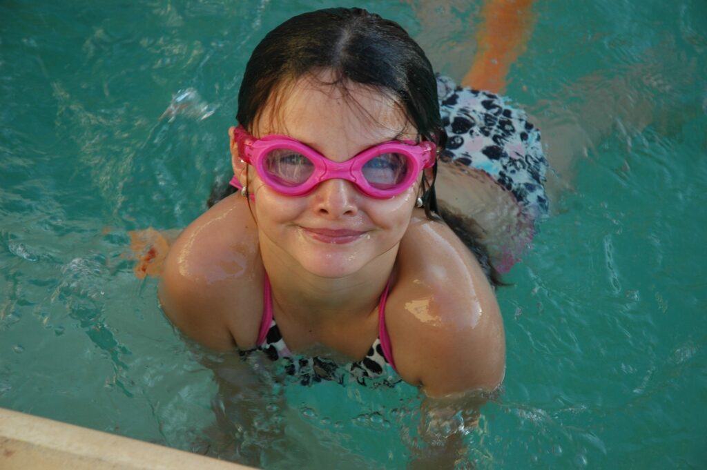 Schwimmen lernendes Mädchen am Beckenrand eines Schwimmbades